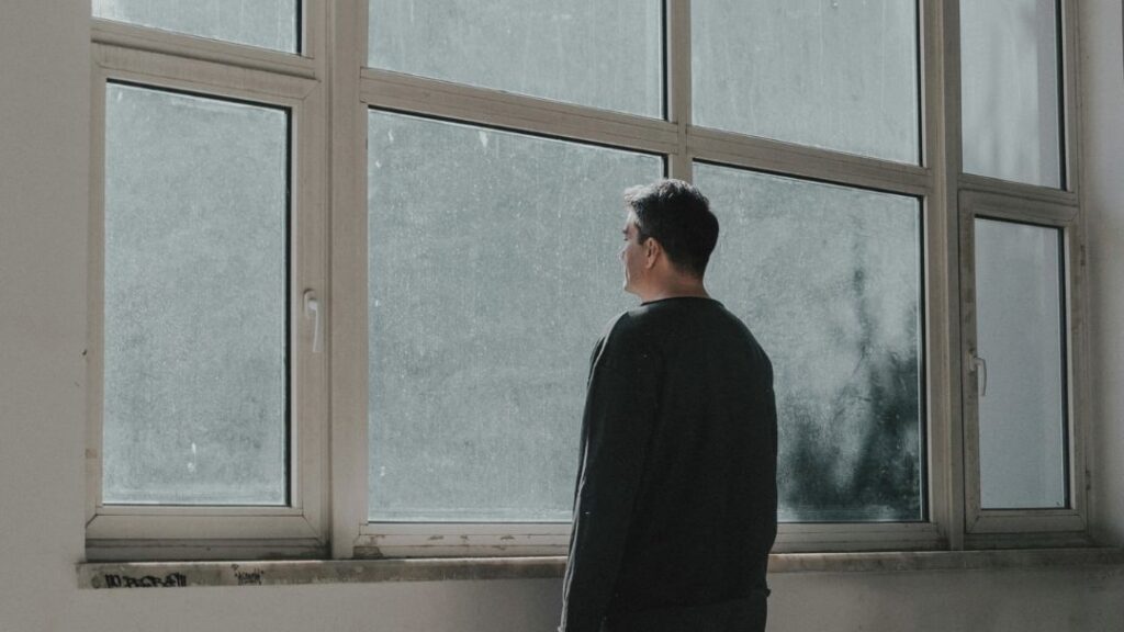 Percepción de mayor dolor de espalda por un bajo estado de ánimo Hombre con bajo estado de ánimo mirando por la ventana en días lluviosos.