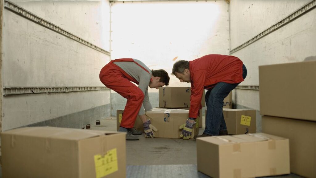 Tareas a evitar en la reincorporación al trabajo tras una cirugía de columna Tareas a evitar en la reincorporación al trabajo después de una cirugía de columna: dos transportistas cogen cajas dentro de una furgoneta.