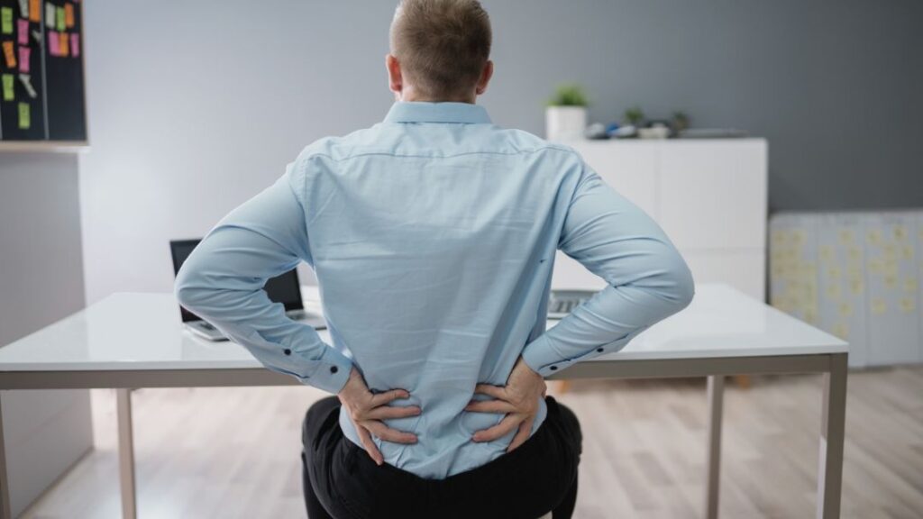 Mala postura frente al ordenador Persona trabajando con mala postura en la oficina, una de las principales causas del dolor lumbar crónico.